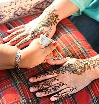 Drawing a design using henna paste on a woman's hand