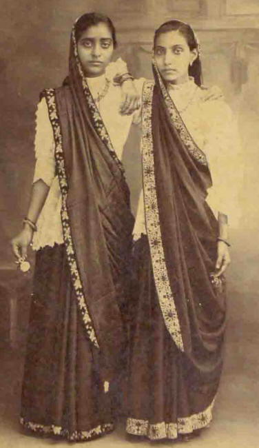 High fashion a century or more ago. Girls / young women wearing sarees with kors. Note the white laced/embrodered blouse that falls over the hips and which may or may not merge with an exposed sudra.